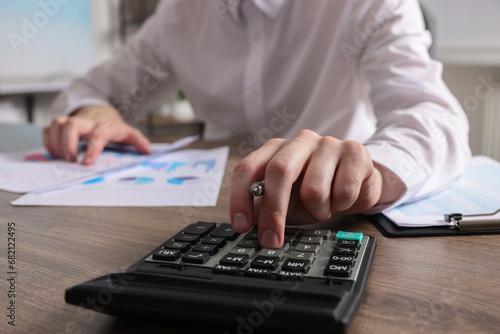 Man using calculator while working with document at wooden table indoors, closeup