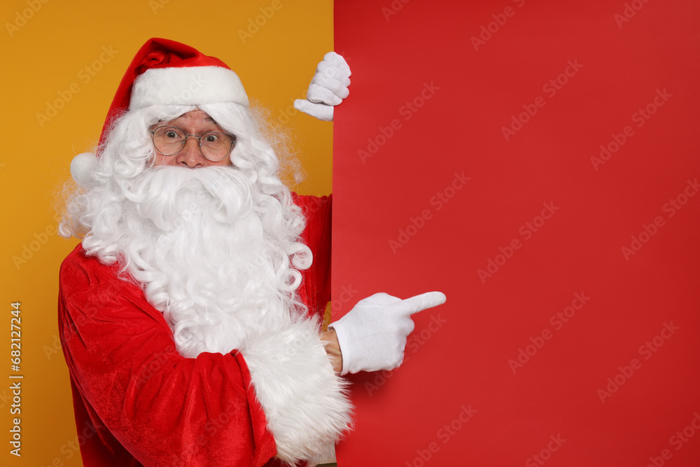 Santa Claus pointing at blank red poster on orange background, space for text Santa Claus pointing at blank red poster on orange background, space for text