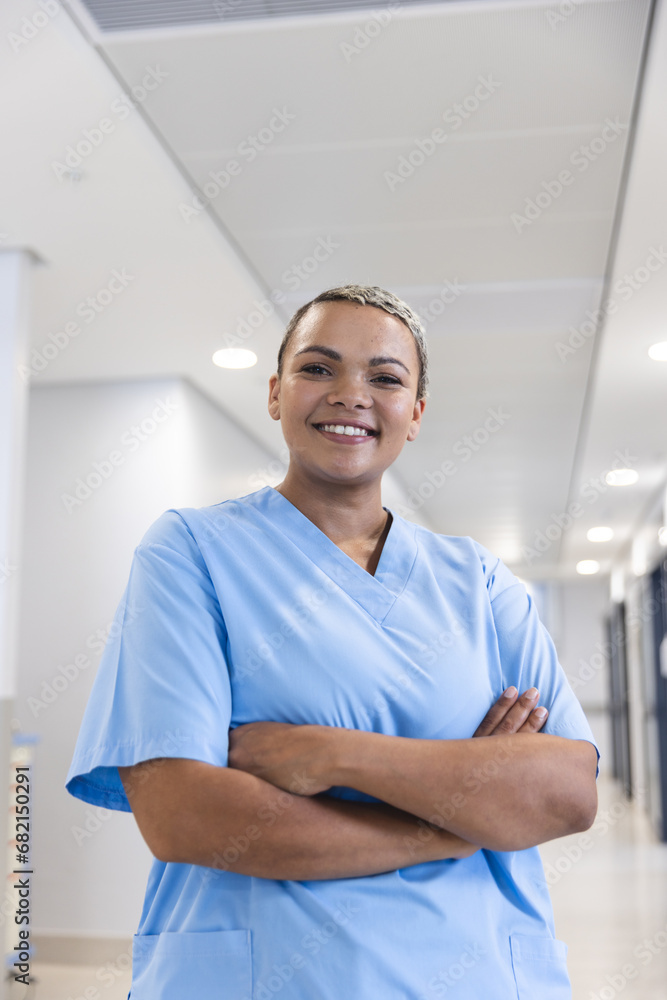 Portrait of happy biracial female doctor wearing scrubs in corridor at hospital, copy space