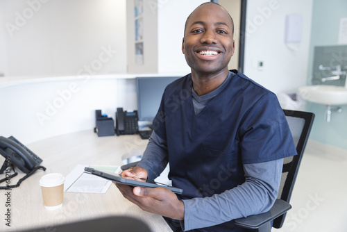 Portrait of happy african american male doctor using tablet at reception desk in hospital photo