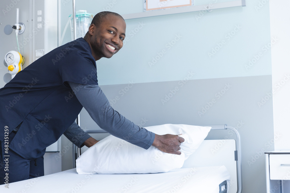 Portrait of happy african american male doctor making bed in hospital room, copy space