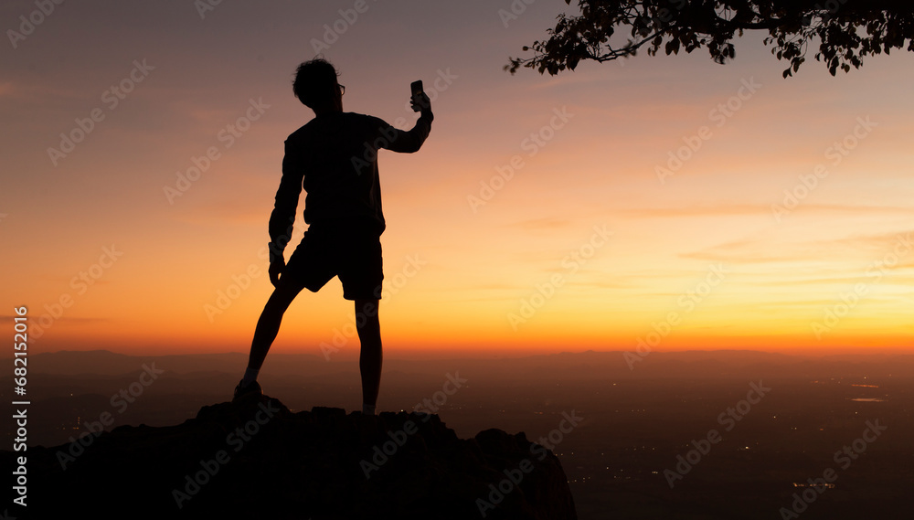 silhouette  man selfie on top of mountain during  happy winning and success hiking at sunset background