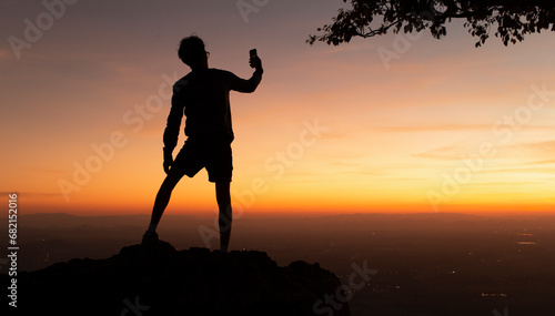 silhouette man selfie on top of mountain during happy winning and success hiking at sunset background