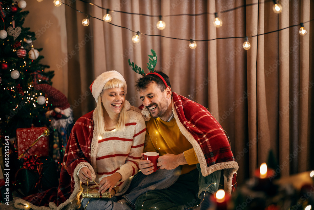 A jolly couple is opening presents and laughing at home on christmas and new year's eve.