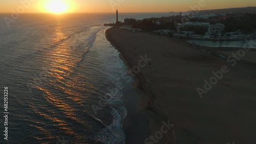 Flying over the shore of Maspalomas beach during sunset with the Maspalomas lighthouse and the pond in the background. photo