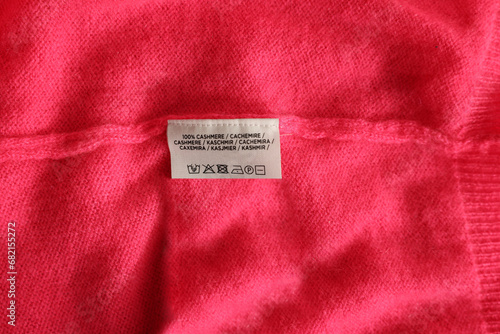 Clothing label in different languages on pink garment, top view