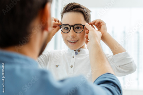 Fototapeta Naklejka Na Ścianę i Meble -  Father wearing glasses to his son at a lens optical shop