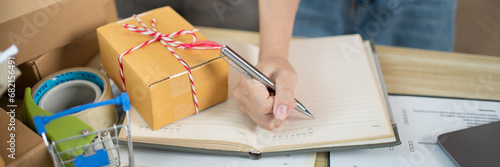 Woman is writing down the customer's details and addresses on the notebook or post box in order to prepare for shipping according to the information, Packing box, Sell online, Freelance working.