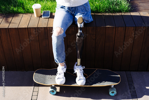 Close up of women prosthetic leg on skateboard in city. Disabled woman with prosthetic leg sitting on wood bench. Woman with leg prosthesis equipment photo