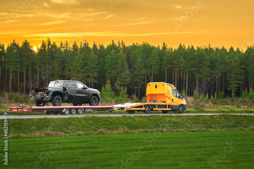 Tow truck with a broken pick-up truck on the interstate highway. Tow truck transporting modern crew cab truck on a road. Roadside Rescue. Car service transportation concept. photo