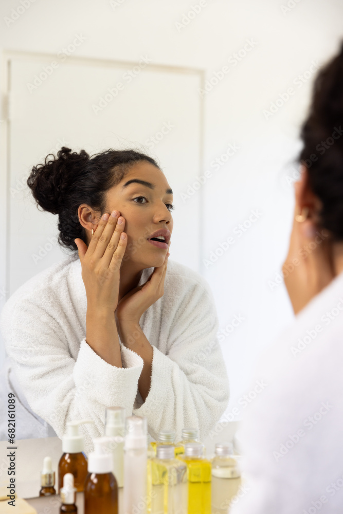 Biracial woman in bathrobe looking in mirror in sunny bathroom Biracial woman in bathrobe looking in mirror in sunny bathroom