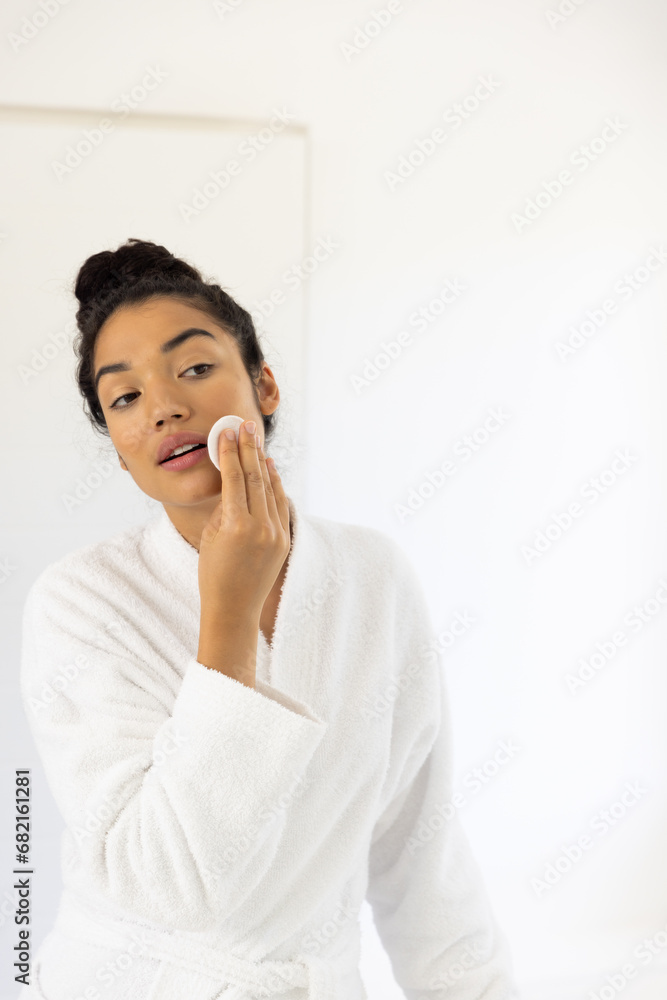 Biracial woman in bathrobe cleansing her face in sunny bathroom Biracial woman in bathrobe cleansing her face in sunny bathroom