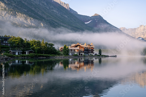 Historic, old style wooden structure on the edge of a mountain lake shrouded in fog and surrounded by trees, Many Glacier Hotel, Swiftcurrent Lake, Glacier National Park, Montana photo