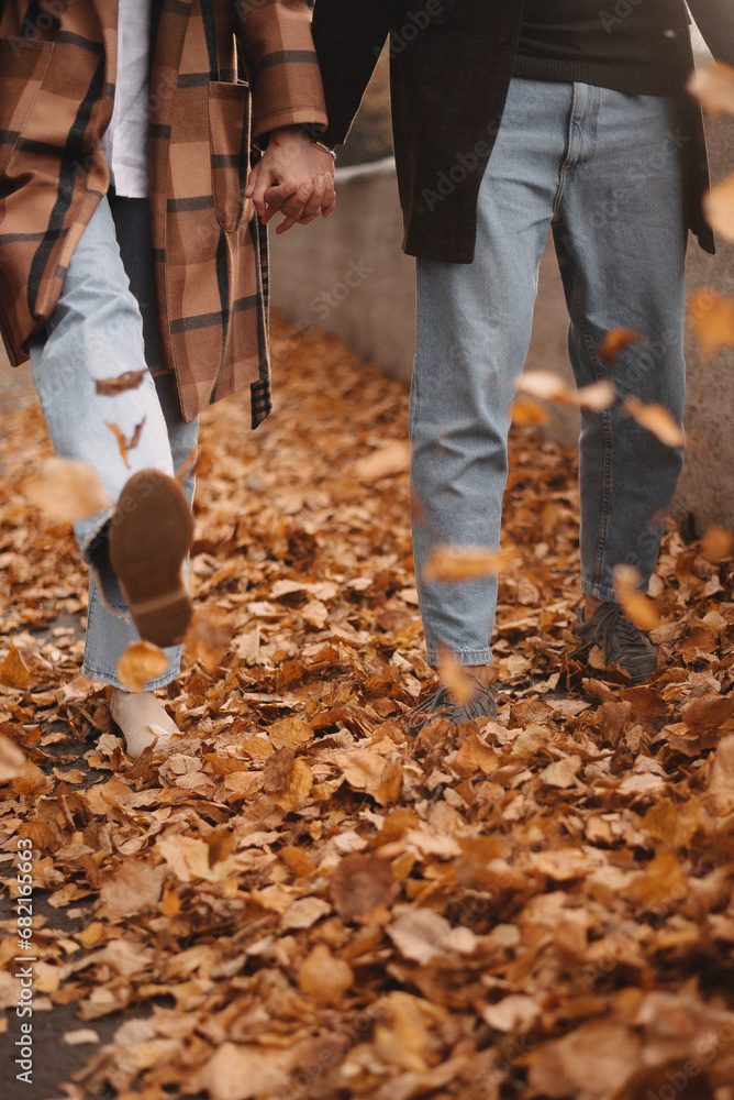 a guy and a girl are walking on autumn leaves . legs close-up on autumn leaves