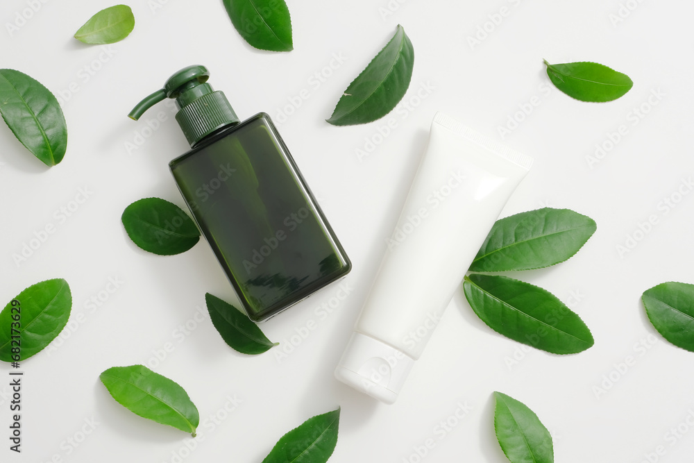 Non-branded shower gel and facial cleanser bottles are displayed. Fresh green tea leaves arranged on a white background. Mockup for cosmetic advertising. Non-branded shower gel and facial cleanser bottles are displayed. Fresh green tea leaves arranged on a white background. Mockup for cosmetic advertising.
