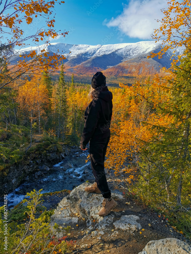 A girl on the background of an autumn Arctic landscape in the Khibiny mountains. Kirovsk, Kola Peninsula, Polar Russia. Autumn colorful forest in the Arctic, mountain hikes and adventures.