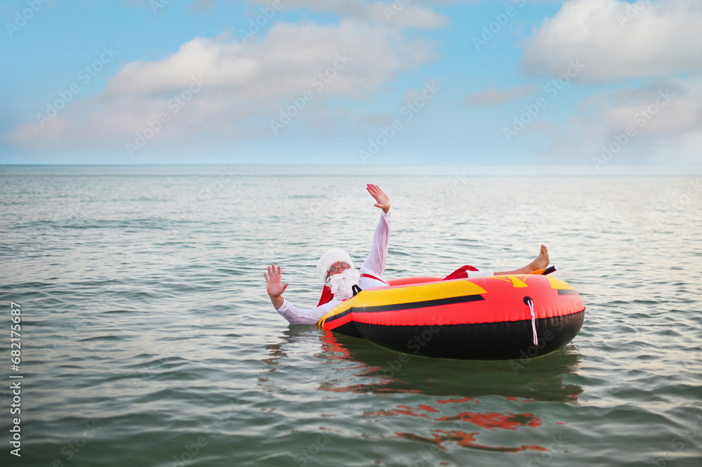 Santa in red suspenders floats on an inflatable boat against the background of the sea. Santa in red suspenders floats on an inflatable boat against the background of the sea.