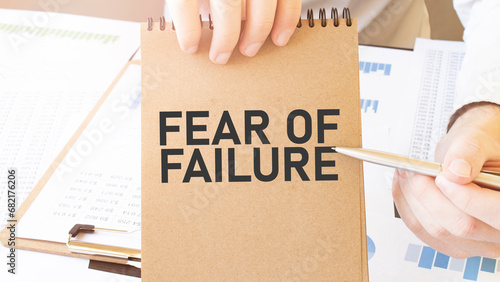 Text FEAR OF FAILURE on brown paper notepad in businessman hands on the table with diagram. Business concept