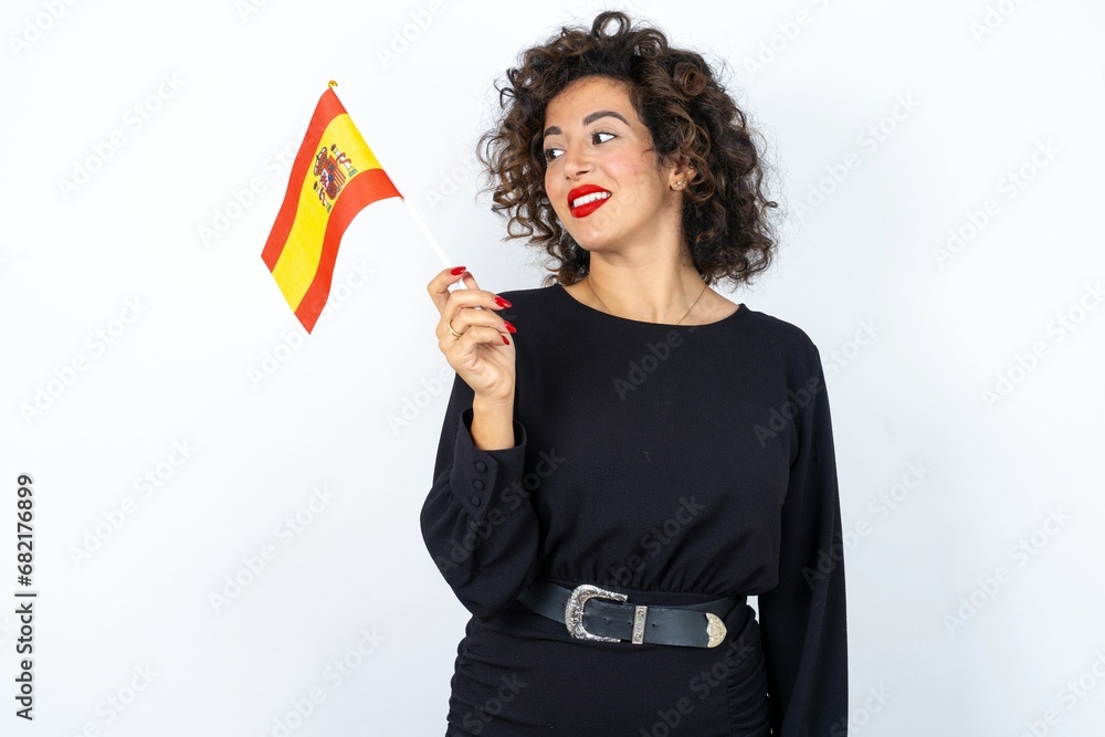 Young beautiful woman with curly hair wearing black dress and Spanish flag feeling excited and confident. Young beautiful woman with curly hair wearing black dress and Spanish flag feeling excited and confident.