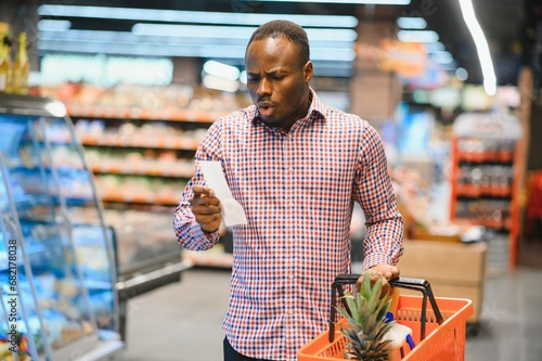Surprised African-American man looks at receipt total in sales check holding paper bag photo