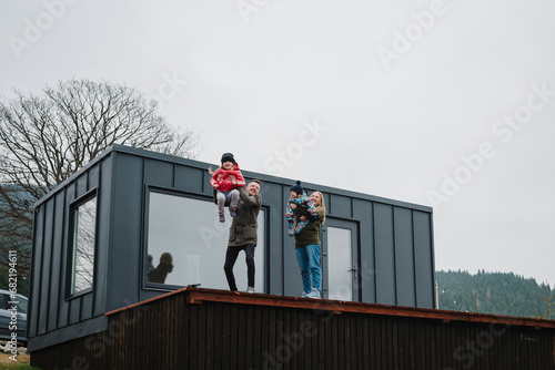 Wallpaper Mural Mother, father throws up kids in the sky on terrace on an autumn day. Family vacation with children in mountains. People stand in backyard of country house. Mom, dad, daughter, son enjoy time together Torontodigital.ca