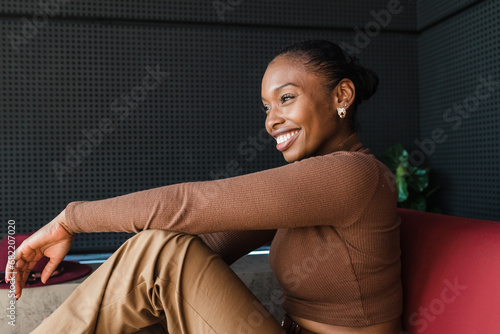 Cheerful stylish black woman sitting on couch