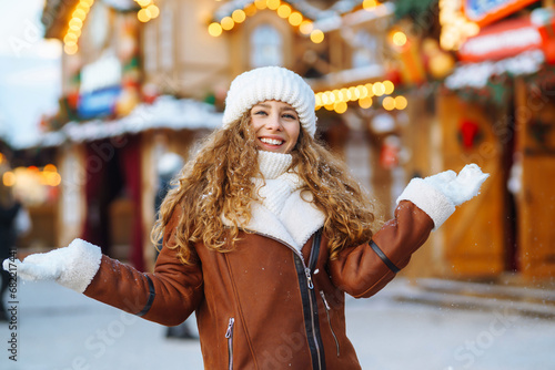 Happy woman in mittens walks on the snowy street of the Christmas market. Young female tourist enjoying snowy weather outdoors. Holiday concept, walk.