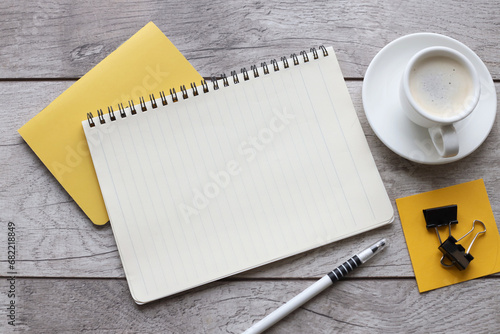Blank notepad on yellow notepad and cup of coffee on wooden table in office