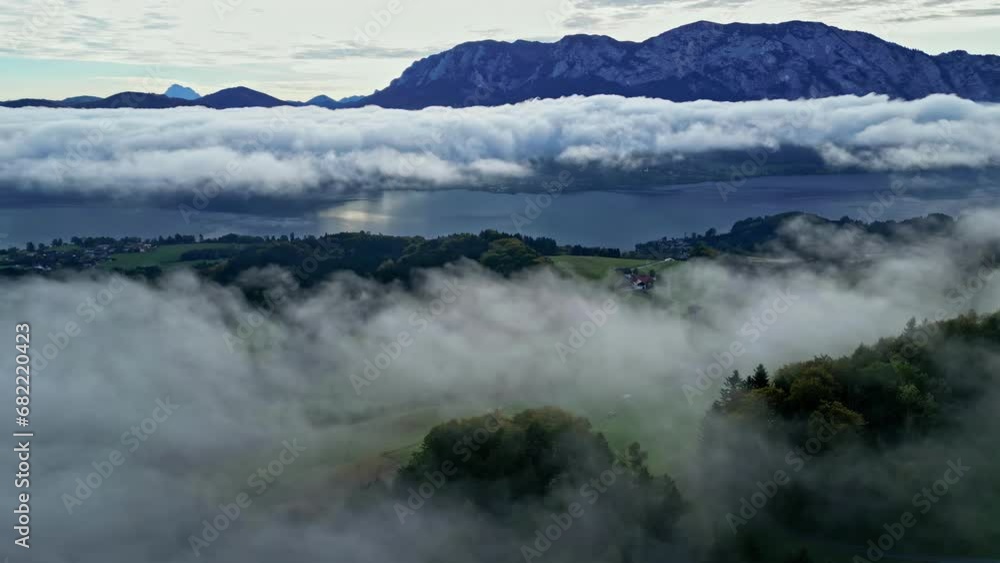 Beautiful aerial drone shot over a forest through white clouds with mountain range in the background during evening time. Beautiful aerial drone shot over a forest through white clouds with mountain range in the background during evening time.