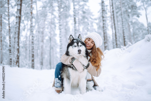 Beautiful young woman walks through the winter forest with her dog. A young woman with her pet on an adventure. Friendship concept, pets. Friendship between a woman and a dog.  © maxbelchenko