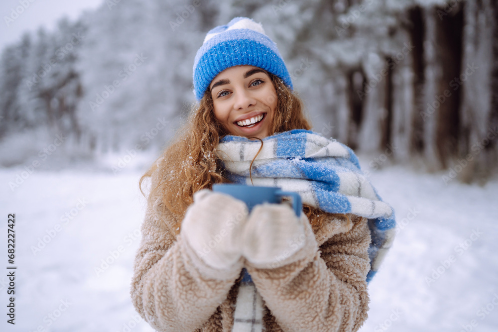 A young woman with a thermos and a cup of coffee in her hands enjoys the first snow in the winter forest. Vacation concept, nature. A young woman with a thermos and a cup of coffee in her hands enjoys the first snow in the winter forest. Vacation concept, nature.
