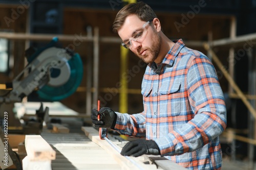 Professional carpenter using sawing machine for cutting wooden board at sawmill. Skilled cabinet maker working with electric circular saw at woodworking workshop. Man joiner, wood production workbench