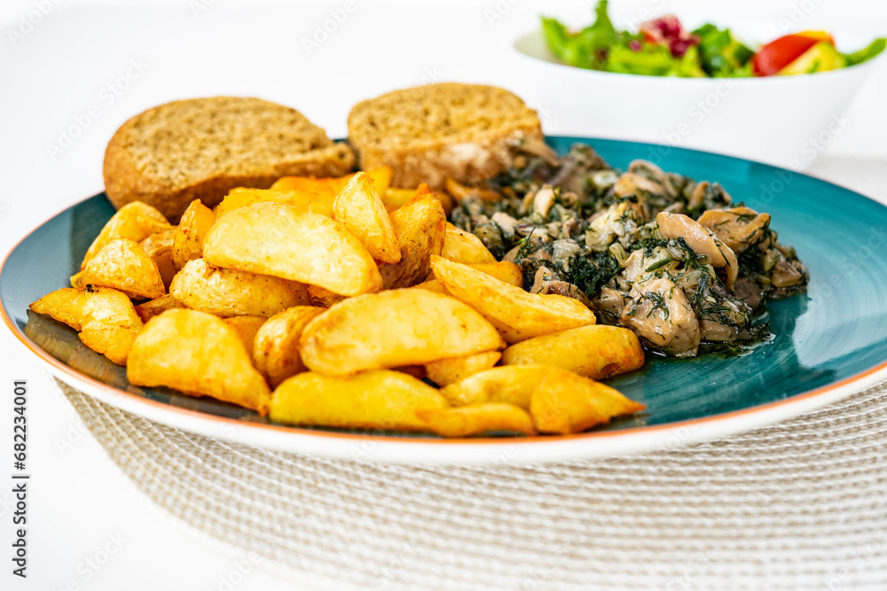 Wedges potatoes with pan fried mushrooms with onion, garlic and dill, near toast, on a green ceramic plate and vegetables salad. Home cooking, healthy eating, vegetarian dish Wedges potatoes with pan fried mushrooms with onion, garlic and dill, near toast, on a green ceramic plate and vegetables salad. Home cooking, healthy eating, vegetarian dish