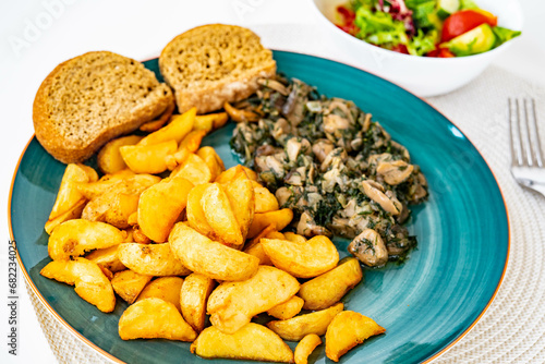 Wedges potatoes with pan fried mushrooms with onion, garlic and dill, near toast, on a green ceramic plate and vegetables salad. Home cooking, healthy eating, vegetarian dish