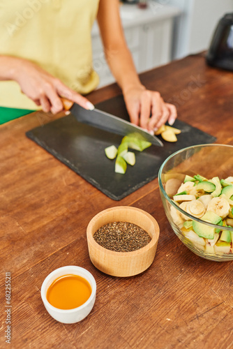 cropped woman cutting fresh fruits while preparing vegetarian salad near honey and sesame seeds