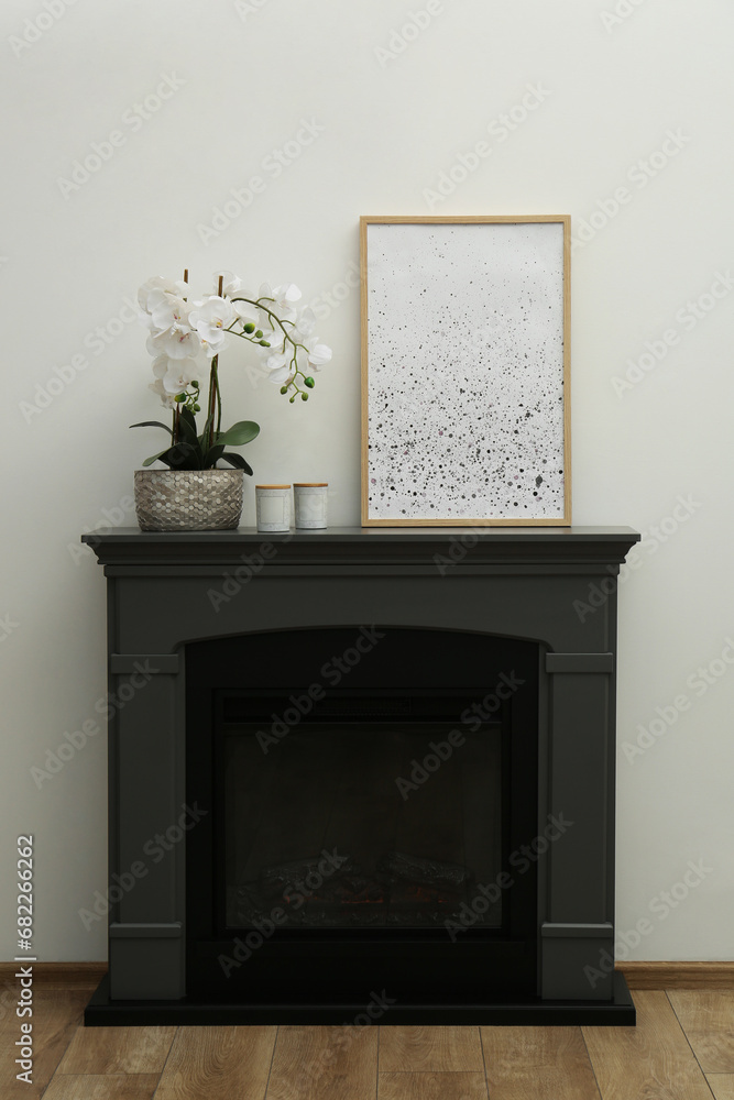 Picture frame, candles and orchid on fireplace near white wall indoors. Interior design Picture frame, candles and orchid on fireplace near white wall indoors. Interior design
