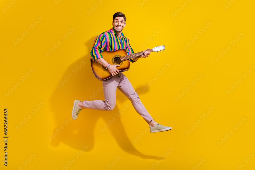 Full size photo of young man professional coach music tutor jumping hold guitar instrument and jumping isolated on yellow color background Full size photo of young man professional coach music tutor jumping hold guitar instrument and jumping isolated on yellow color background