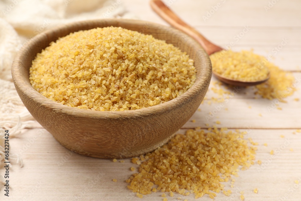 Bowl and spoon with raw bulgur on light wooden table Bowl and spoon with raw bulgur on light wooden table