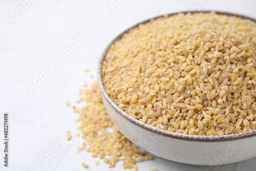 Raw bulgur in bowl on white table, closeup. Space for text