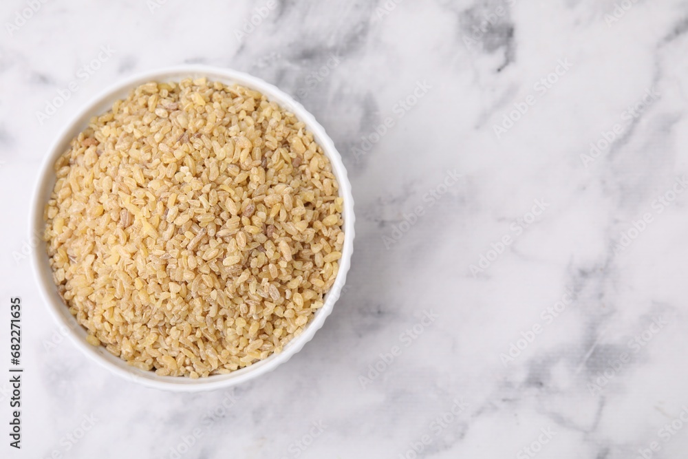 Raw bulgur in bowl on marble table, top view. Space for text Raw bulgur in bowl on marble table, top view. Space for text