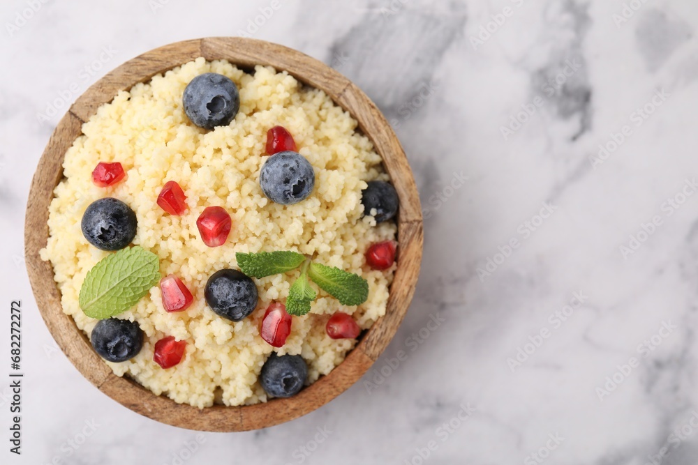 Bowl of tasty couscous with blueberries, pomegranate and mint on white marble table, top view. Space for text Bowl of tasty couscous with blueberries, pomegranate and mint on white marble table, top view. Space for text