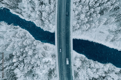 Aerial top view of snow winter road with cars over blue river © nblxer