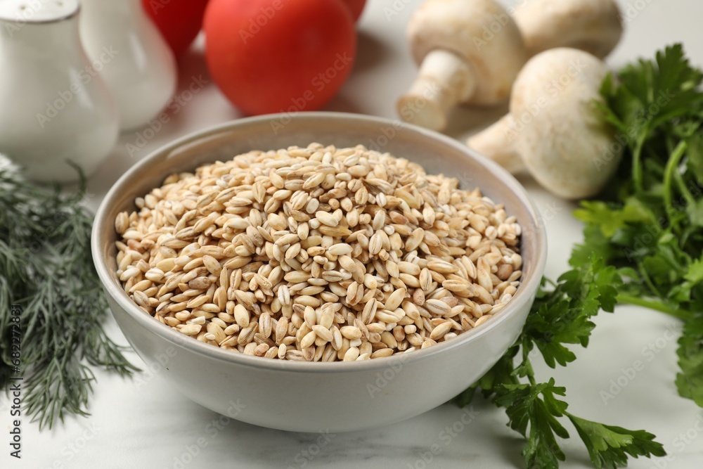 Dry pearl barley in bowl and products on white marble table Dry pearl barley in bowl and products on white marble table