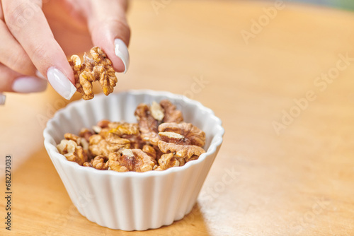 cropped view of female hand taking walnut from white ceramic bowl, high-calorie plant-based food