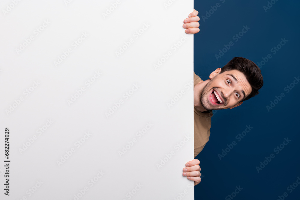 Photo of glad positive man wear stylish clothes look out poster announcement empty blank space isolated on dark blue color background Photo of glad positive man wear stylish clothes look out poster announcement empty blank space isolated on dark blue color background