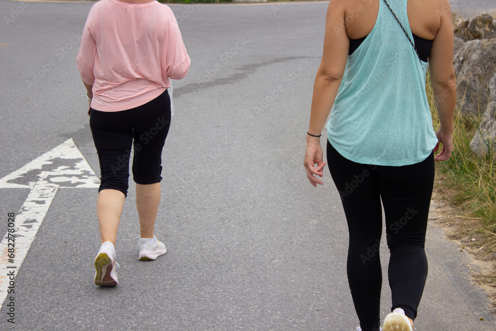 Mother and daughter going for a walk. Back picture of a young woman and older woman with sport clothes. Long and short black leggings. Sleeve-less and long sleeve t-shirts, blue and pink. Mother and daughter going for a walk. Back picture of a young woman and older woman with sport clothes. Long and short black leggings. Sleeve-less and long sleeve t-shirts, blue and pink.