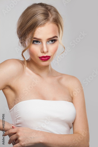 Glamorous woman with makeup and long healthy blonde shiny wavy hair posing against white studio wall background. Emotional fashion beauty portrait