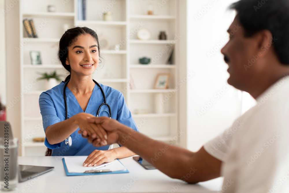 Meeting In Clinic. Smiling Indian Therapist Lady Shaking Hands With Male Patient Meeting In Clinic. Smiling Indian Therapist Lady Shaking Hands With Male Patient