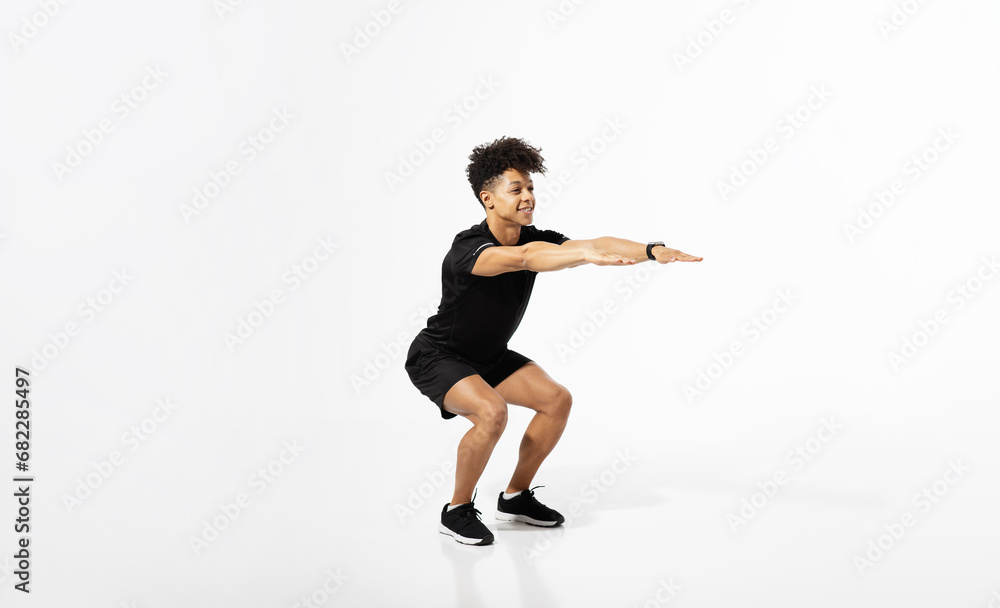 Athletic young man extending arms squatting over white studio background