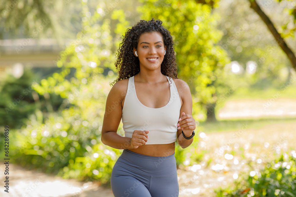 Energetic young woman in fitwear running in park with earbuds Energetic young woman in fitwear running in park with earbuds